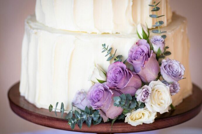 画像：白いシンプルなウエディングケーキと紫のバラの装花