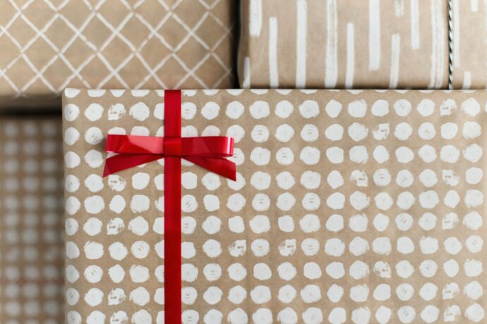 画像：ブラウンのデザイン包装紙に包まれた複数のプレゼントのうち1つに赤いリボンが巻かれている
