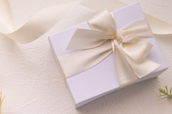 画像：白い背景に白い夫包装紙で包まれ、白いリボンで飾られたプレゼントボックス