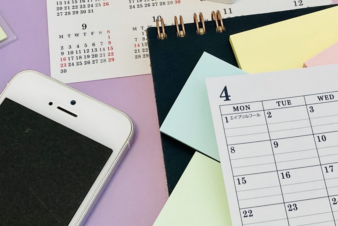 画像：紫の机の上に散らばったスマートフォンやカレンダー、付箋などの文房具類