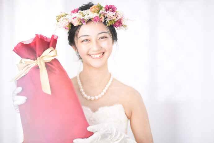 画像：大きな赤いプレゼントの包みを持って微笑みかける花嫁