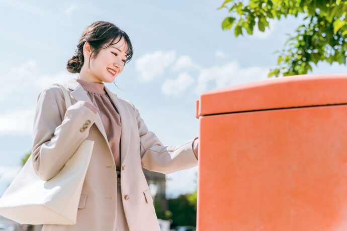 画像：郵便ポストに投函する女性