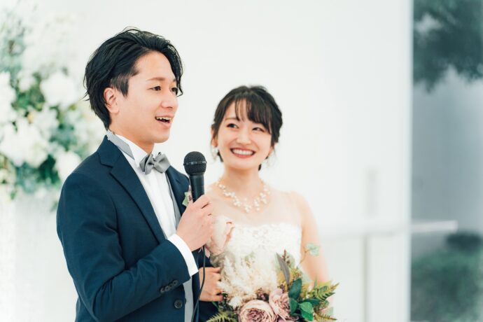 画像：マイクを握り話す新郎と笑顔を向ける新婦