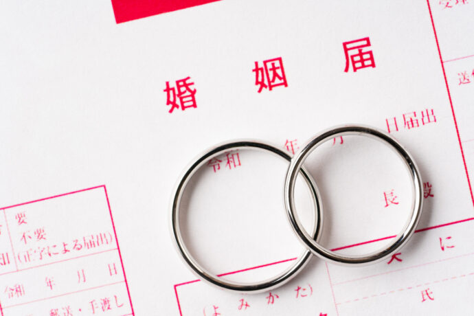 画像：婚姻届けの上に置かれたシンプルな2本の結婚指輪