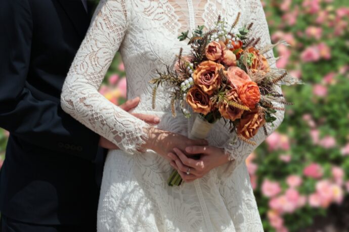 画像：赤いブーケを持つ花嫁と手を回す花婿